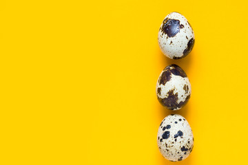 Vertical row of speckled quail eggs on bright yellow background. Easter greeting card poster banner...