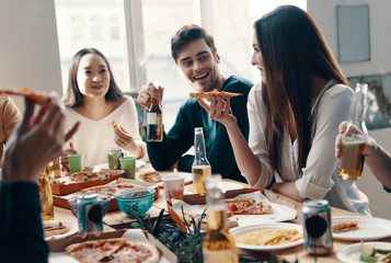 Good food and good friends. Group of young people in casual wear eating pizza and smiling while having a dinner party indoors