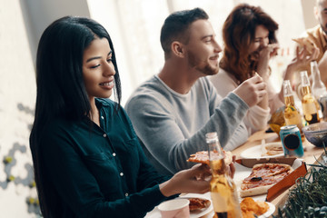 Among best friends. Group of young people in casual wear eating pizza and smiling while having a dinner party indoors