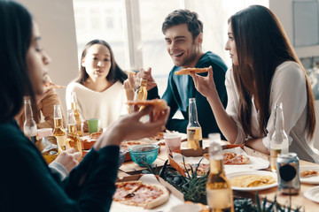 Great food and great people. Group of young people in casual wear eating pizza and smiling while having a dinner party indoors