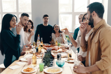 Enjoying time with friends. Group of young people in casual wear eating pizza and smiling while having a dinner party indoors