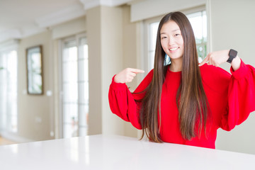 Beautiful Asian woman wearing red sweater on white table looking confident with smile on face,...