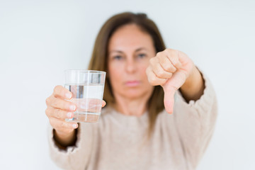 Middle age woman drinking glass of water isolated background with angry face, negative sign showing dislike with thumbs down, rejection concept