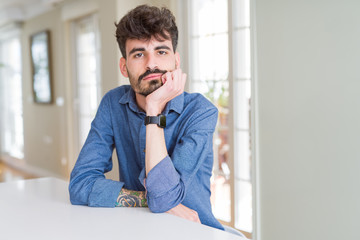Fototapeta premium Young man wearing casual shirt sitting on white table thinking looking tired and bored with depression problems with crossed arms.