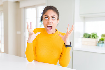 Beautiful young african american woman with afro hair crazy and mad shouting and yelling with aggressive expression and arms raised. Frustration concept.
