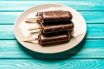 chocolate popsicle ice cream with a stick on a plate, on a blue wooden table, top view