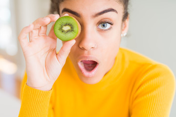 Young african american girl eating green kiwi scared in shock with a surprise face, afraid and excited with fear expression