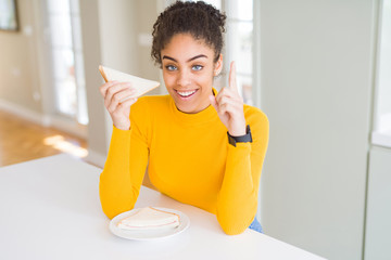 Young african american woman eating a sandwich as healthy snack surprised with an idea or question pointing finger with happy face, number one