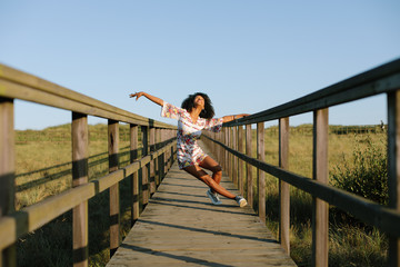 Fototapeta na wymiar Joyful woman dancing and having fun on vacation. Spring or summer outdoor relaxing leisure. Afro hair young black female.