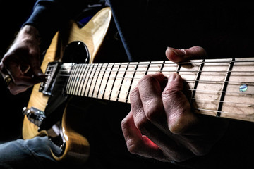 Guitarist playing a natural wood electric guitar in moody light with focus on fingers of fret hand...