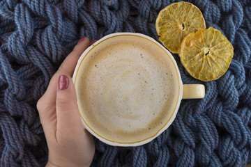 A Cup of coffee in a cozy style on a blue knitted blanket background. Slices of dried orange.