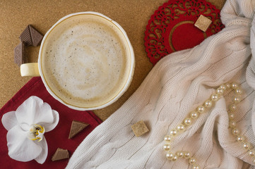 A Cup of coffee in a cozy style on a cork background and a white knitted blanket. Black and red colors. Flat lay.