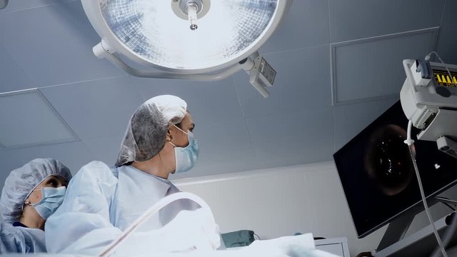 Young doctor monitoring surgery process at monitor using the endoscopy instrument in operation room. Surgeon professional woman work with technology tools and operating patient under the lamp
