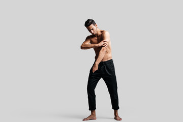Dark-haired handsome young dancer with  bare torso wearing a black pants makes dancing movements on a white background