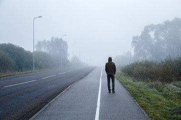 Young man alone walking on sidewalk in mist of early morning. Foggy air. Go away. Back view.
