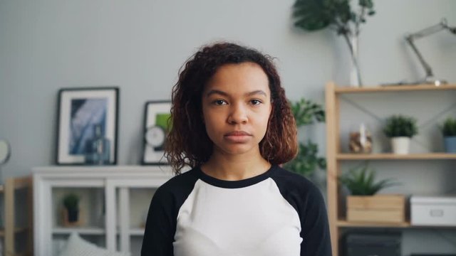Slow motion portrait of unemotional African American woman looking at camera standing alone at home with straight face. Apartment, people and interior concept.