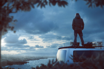 Junger Mann steht auf dem Dach eines Camper Van