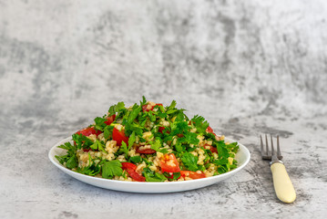 Tabbouleh salad with bulgur, parsley, spring onion and tomato in bowl on grey background. Top view. WIth copy space