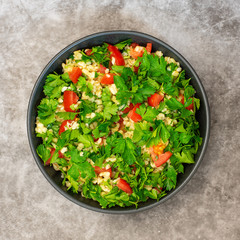 Tabbouleh salad with bulgur, parsley, spring onion and tomato in bowl on grey background. Top view