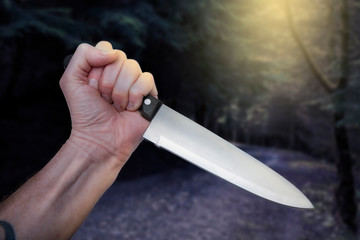 Horror scene of murderer or maniac’s hand with large butcher knife in creepy woods scanario...