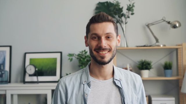 Portrait of happy good-looking guy smiling and looking at camera standing at home alone whearing casual clothing. Attractive people and positive emotions concept.