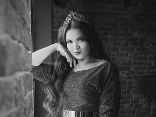 monochrome (black and white) portrait of beautiful young pretty cute woman princess (queen) in long purple queen's dress and crown, with long hair and make up indoor in minimalistic interior