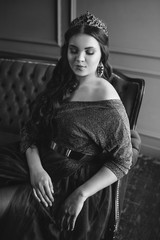 monochrome (black and white) portrait of beautiful young pretty cute woman princess (queen) in long purple queen's dress and crown, with long hair and make up indoor in minimalistic interior