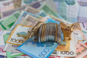 Bronze figures of a bull and a bear near metal coins on the background of paper money. Blur...