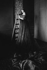 portrait of beautiful young pretty cute woman princess (queen) in long purple queen's dress and crown, with long hair and make up indoor in minimalistic interior