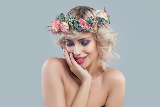 Smiling model in flowers. Beautiful young woman with short blonde curly hair and bright makeup