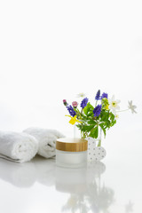 Obraz na płótnie Canvas handtücher neben einer Cremedose vor weißem Hintergrund und Blumen in einer Vase.