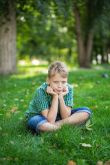 Fototapeta premium Vertical photography of white kid sitting on green grass outdoors at urban park. 