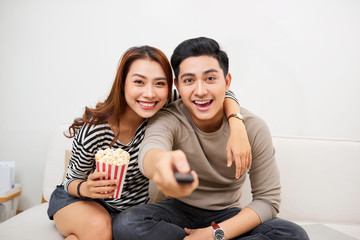 Young couple watching tv, eating pop-corn and having fun together.