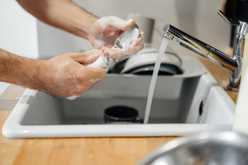 Homework, male hands with a sponge in the foam wash spoons in the sink in the kitchen detergent.