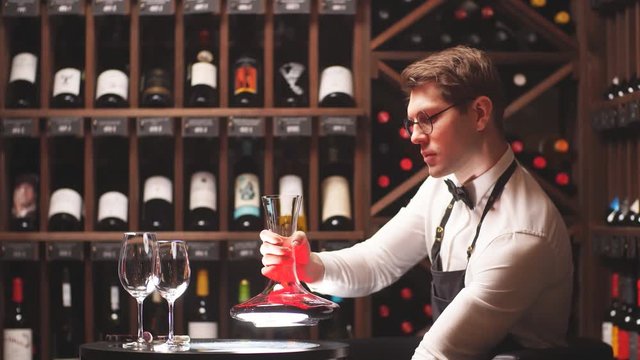 Wine taster or degustator mixing red wine into carafe to make perfect color on background with wine bottles racks in wine house.