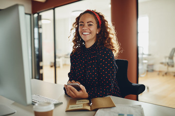 Smiling young businesswoman using a cellphone at her office desk