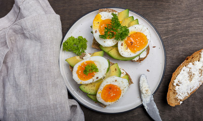 Toast with cream cheese, avocado and eggs on plate at wooden background
