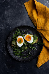 Boiled egg on arugula salad with grain bread on black plate with orange napkin