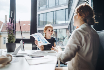 A businesswoman with small daughter sitting in an office, working.