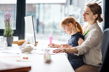 A businesswoman with small daughter sitting in an office, working.