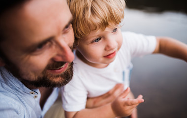 A close-up of father with a toddler boy outdoors by the river in summer.