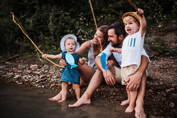 A young family with two toddler children outdoors by the river in summer.