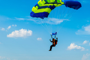 Male skydiver flies under the wing of the parachute, descending and coming in to land closer to the ground on a background of blue sky, white clouds