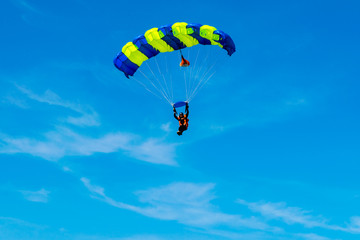 Male skydiver flies under the wing of the parachute, descending and coming in to land closer to the ground on a background of blue sky, white clouds