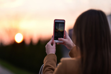 girl takes photo a city sunset on her smartphone