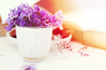 Still life with violet in white cup, old books and date fruits in a plate. Romantic floral background.