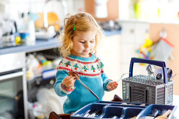 Cute little toddler girl helping in the kitchen with dish washing machine. Happy healthy blonde...