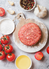 Raw minced homemade grill beef burger with spices and herbs. Top view.On top of chopping board and kitchen table background. With pepper salt and garlic.