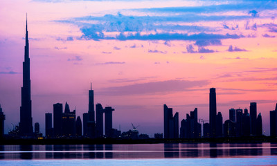 Fototapeta na wymiar Stunning view of the silhouette of the Dubai skyline during sunset with the magnificent Burj Khalifa and many other buildings and skyscrapers reflected on a silky smooth water. Dubai.