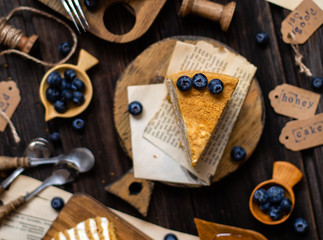 Delicious homemade slices of russian honey cake medovik with white cream, blueberries on top on wooden boards on rustic table 